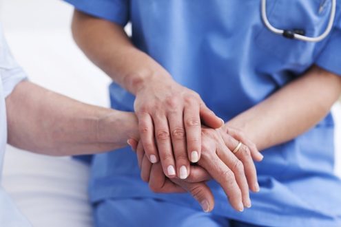 Close up of a nurse touching hand of a patient in hospital ward